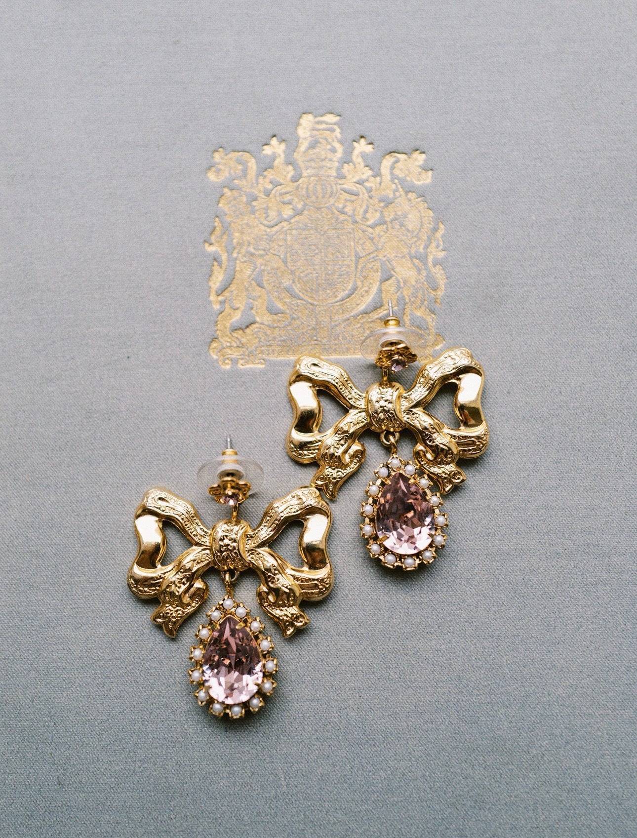 Gold bow-shaped earrings with pink gemstones on a gray background | EDEN LUXE Bridal