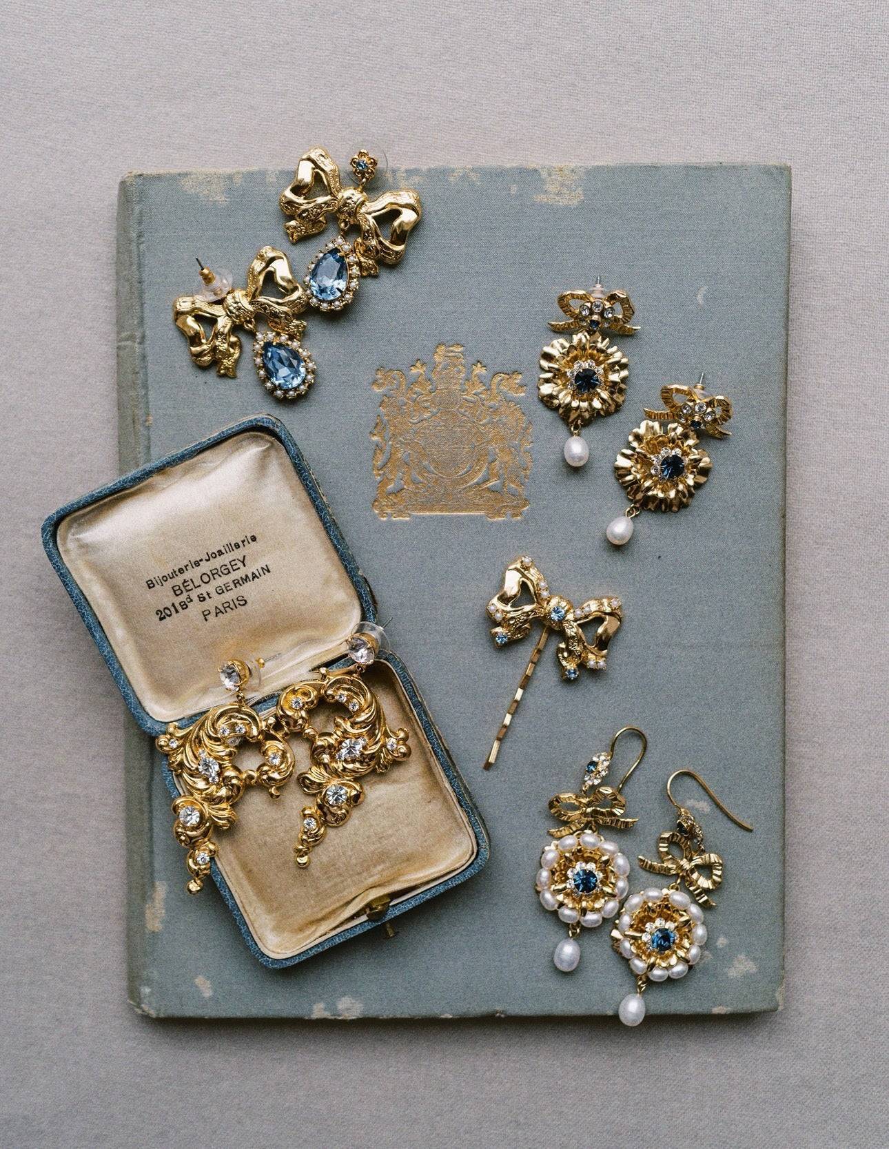 Collection of gold jewelry including earrings and a brooch on an old book | EDEN LUXE Bridal