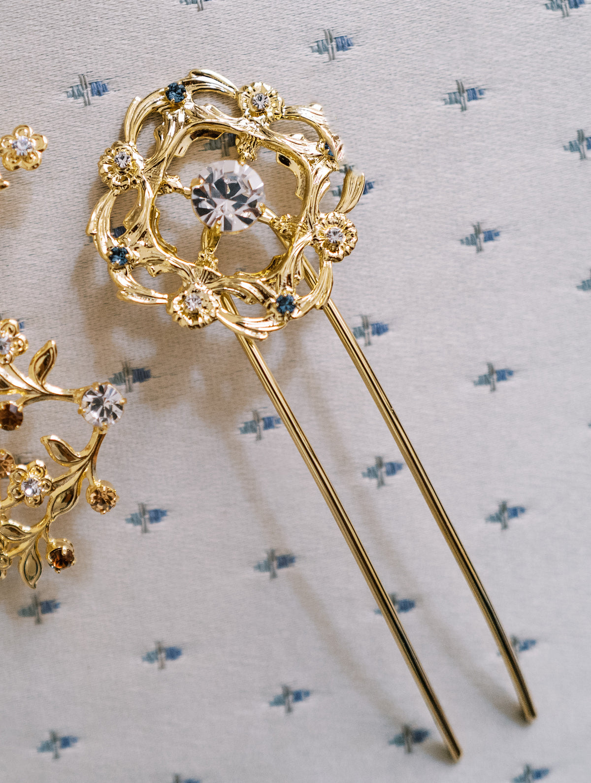 Close-up of the Martha Hairpin, gold buckle-shaped hair pin with a clear Swarovski crystal center and French blue accents, Sophie Kaye x EDEN LUXE Revolution Collection | EDEN LUXE Bridal