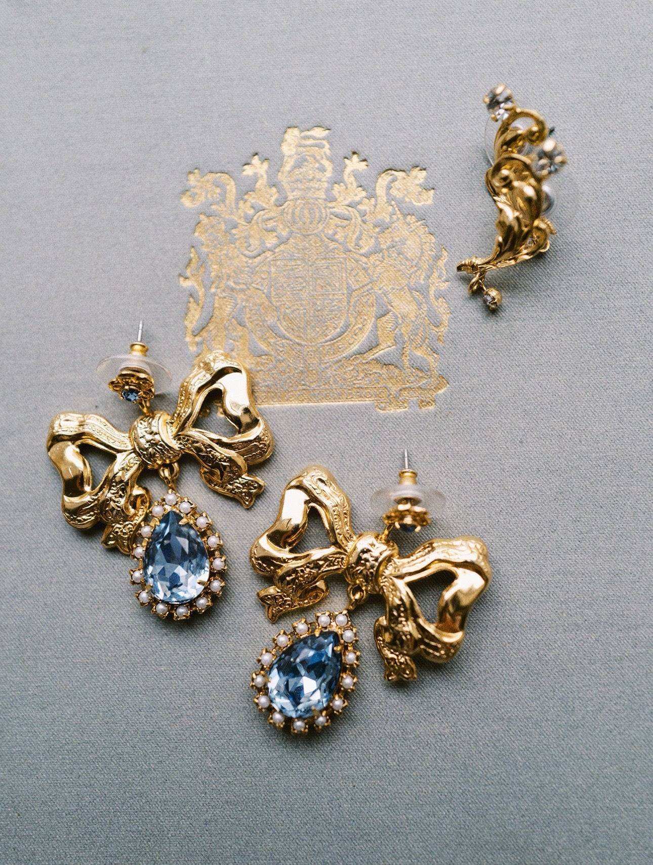 Gold bow-shaped earrings with blue gemstones on a gray background