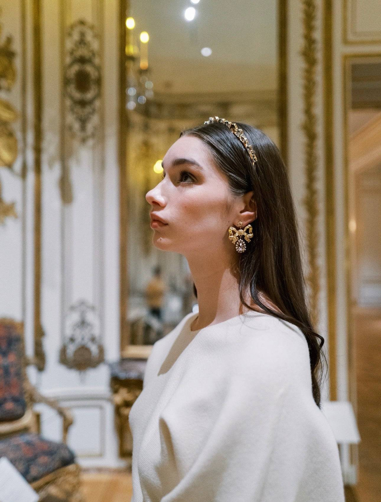 Woman wearing gold bow earrings and a headband in an elegant interior setting