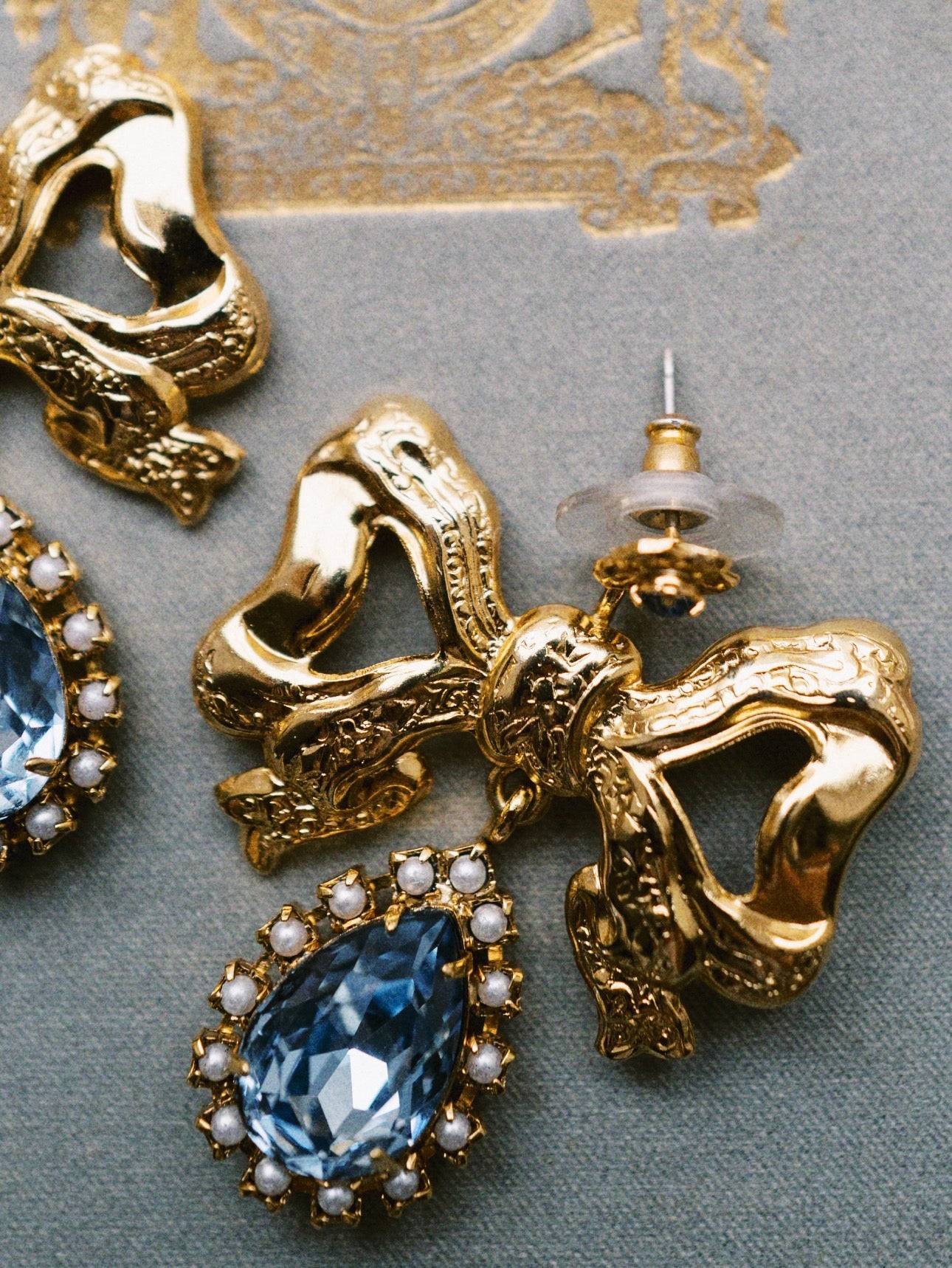 Gold earrings with blue gemstones and pearl accents on a gray surface