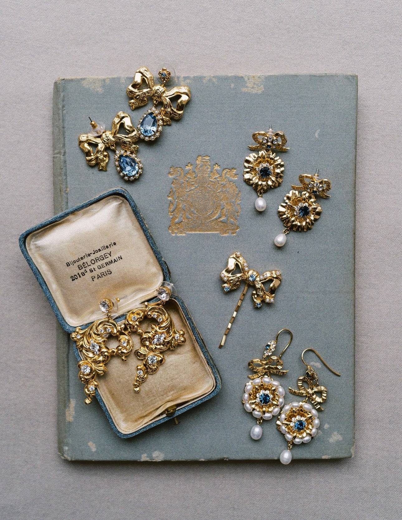 Collection of gold jewelry including earrings and a brooch on an old book | EDEN LUXE Bridal 