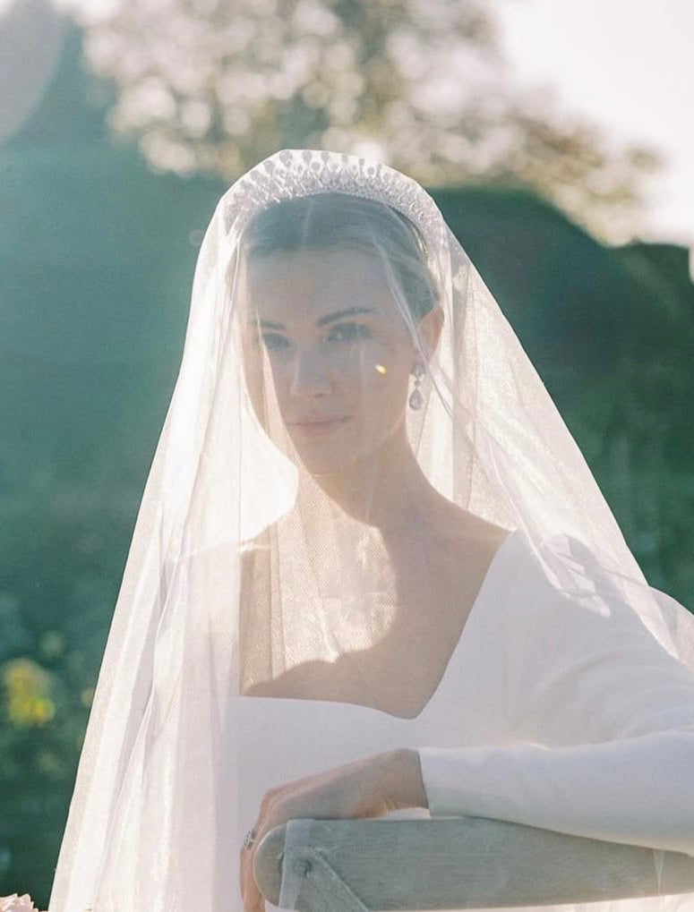 Woman wearing a tiara and a white wedding dress with a veil against a blurred natural background
