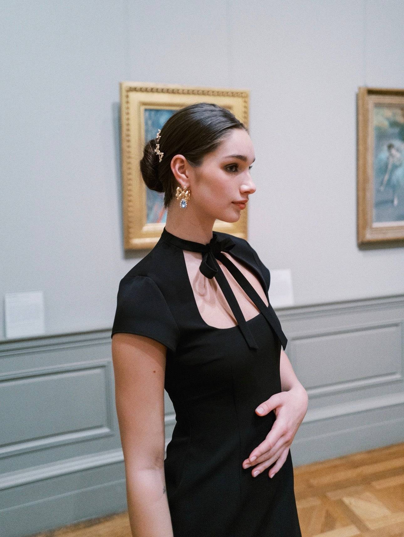 Woman in a black dress standing in an art gallery with paintings on the wall.
