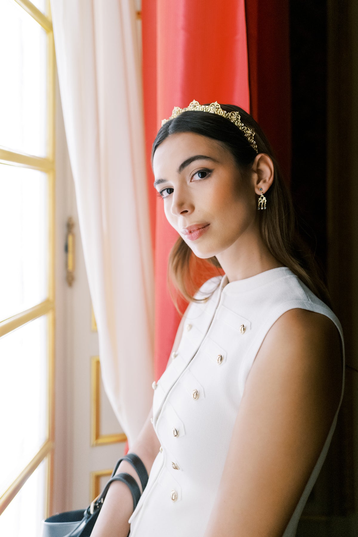 Antoinette Halo Everyday Tiara portrait by a window with red silk curtains at The Metropolitan Museum of Art, 14k gold plated Rococo headband by Sophie Kaye x EDEN LUXE | EDEN LUXE Bridal