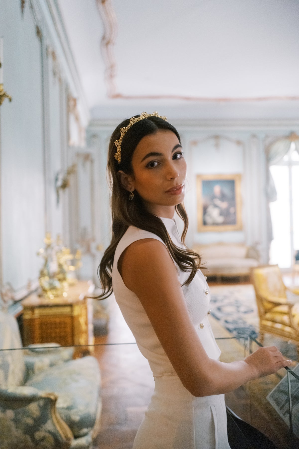 Model in white wearing the Antoinette Halo gold crystal headband beside Rococo gilt furniture at The Metropolitan Museum of Art, Sophie Kaye x EDEN LUXE Revolution Collection | EDEN LUXE Bridal